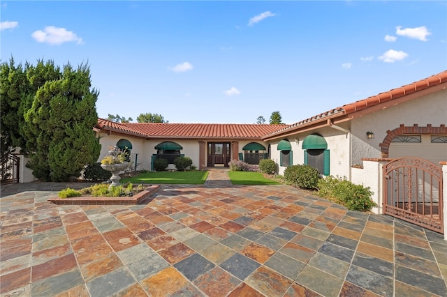 mediterranean / spanish home with a gate, stucco siding, and a tiled roof