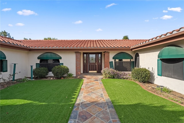 view of exterior entry with a tiled roof, a yard, stucco siding, and brick siding