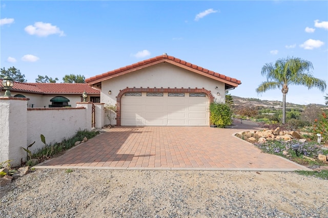 mediterranean / spanish house with a garage, stucco siding, a tile roof, and decorative driveway