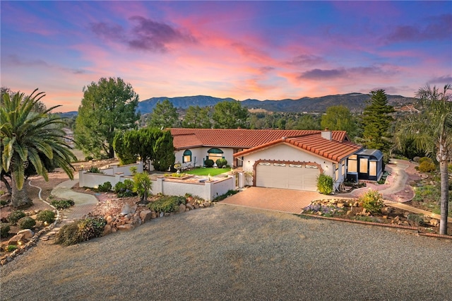 mediterranean / spanish-style home featuring an attached garage, a tile roof, stucco siding, a mountain view, and decorative driveway