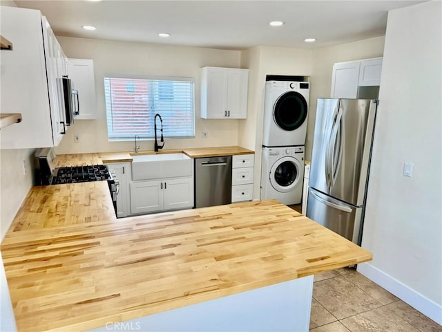 kitchen featuring a peninsula, a sink, stacked washer / dryer, wooden counters, and appliances with stainless steel finishes