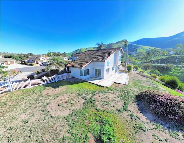 rear view of house featuring fence, a lawn, a tile roof, stucco siding, and a mountain view