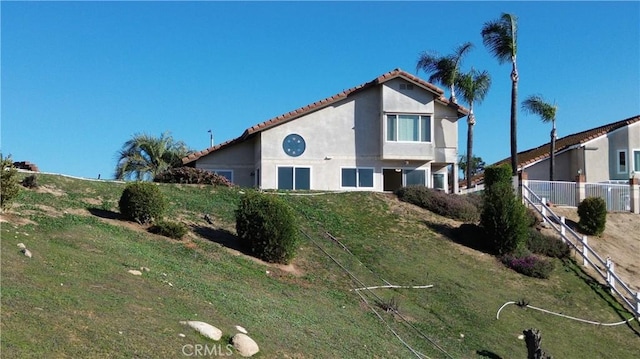 view of front of property featuring a tile roof, a front yard, stucco siding, and fence