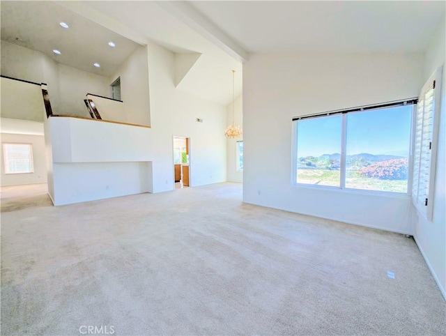 unfurnished living room with plenty of natural light, high vaulted ceiling, carpet floors, and a chandelier
