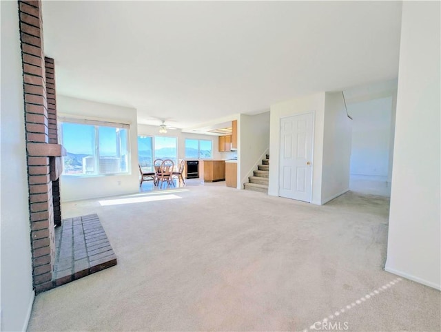 unfurnished living room featuring carpet, baseboards, ceiling fan, a fireplace, and stairway