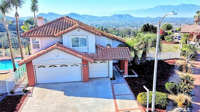 mediterranean / spanish-style home with a tile roof, concrete driveway, fence, an attached garage, and a chimney