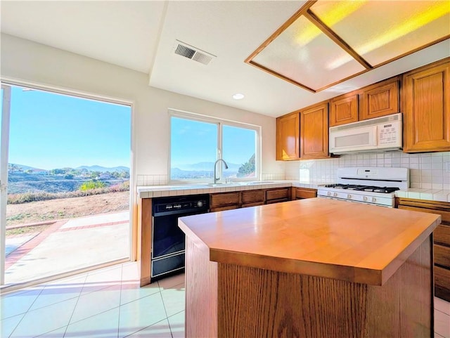kitchen with tile counters, brown cabinetry, white appliances, visible vents, and decorative backsplash
