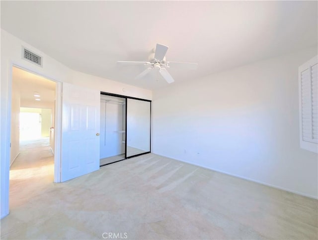unfurnished bedroom featuring light colored carpet, visible vents, a closet, and a ceiling fan