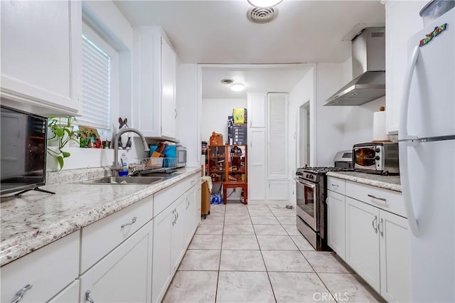 kitchen featuring freestanding refrigerator, wall chimney exhaust hood, stainless steel gas range, a sink, and a toaster