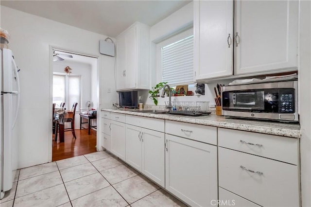 kitchen with a sink, freestanding refrigerator, stainless steel microwave, white cabinetry, and light tile patterned flooring