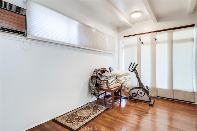 interior space with a wall mounted AC, beamed ceiling, and wood finished floors