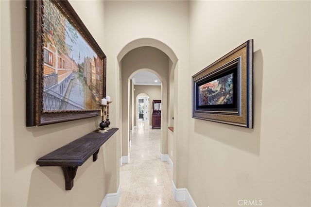 hallway featuring arched walkways, marble finish floor, and baseboards