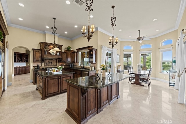 kitchen with arched walkways, a towering ceiling, ornamental molding, and a kitchen island with sink