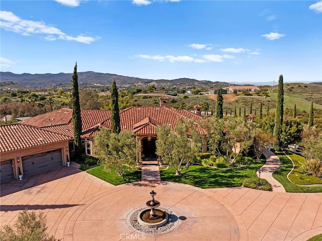 mediterranean / spanish home featuring a tiled roof, a front lawn, an attached garage, a mountain view, and concrete driveway