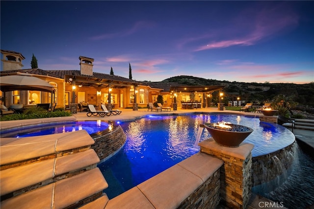 pool at dusk with a pool with connected hot tub and a fire pit