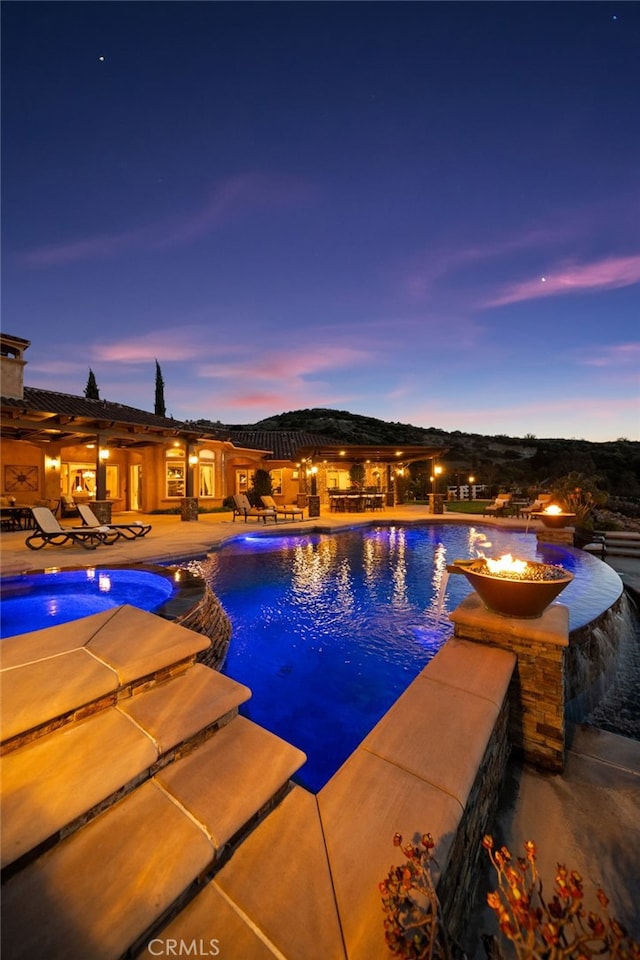 pool at dusk featuring a patio and a pool with connected hot tub