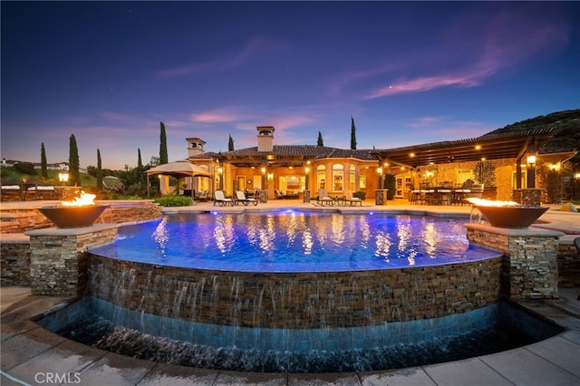 pool at dusk with an outdoor pool, a fire pit, a hot tub, and a patio area