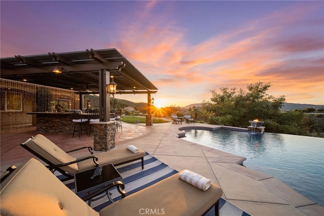 view of swimming pool with a pergola, outdoor dry bar, a patio area, and an infinity pool