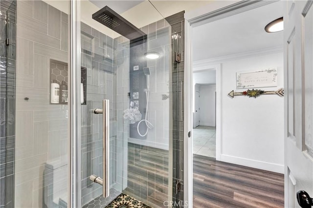 bathroom featuring a tile shower, crown molding, wood finished floors, and baseboards