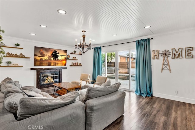 living room with dark wood finished floors, an inviting chandelier, ornamental molding, and a glass covered fireplace