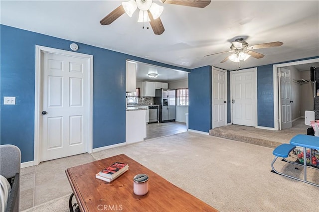living area featuring a ceiling fan, light carpet, baseboards, and light tile patterned floors