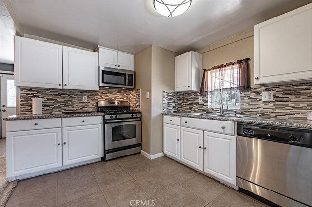 kitchen with backsplash, a sink, light tile patterned floors, stainless steel appliances, and white cabinets