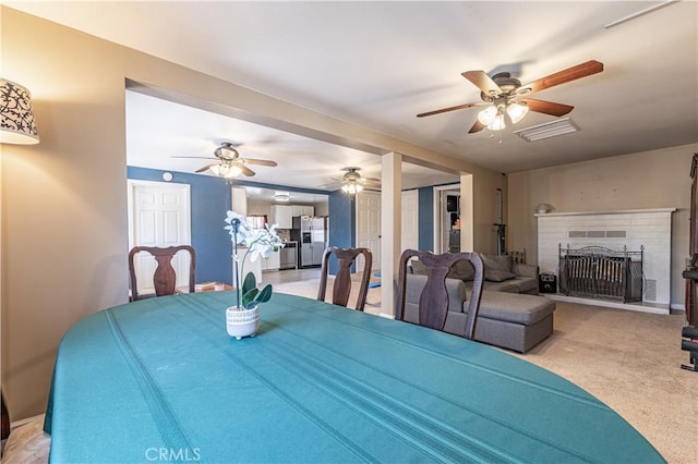 dining area featuring a brick fireplace, visible vents, light carpet, and ceiling fan