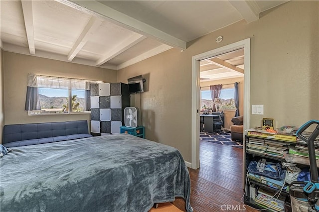 bedroom featuring baseboards, beamed ceiling, wood finished floors, and a textured wall