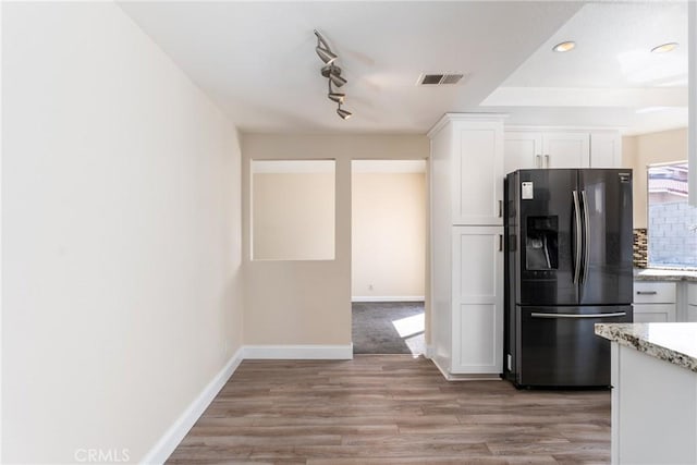1076 N Ironwood Ave, Rialto, CA 92376 - kitchen with black fridge with ice dispenser, white cabinetry, light stone countertops, baseboards, and visible vents