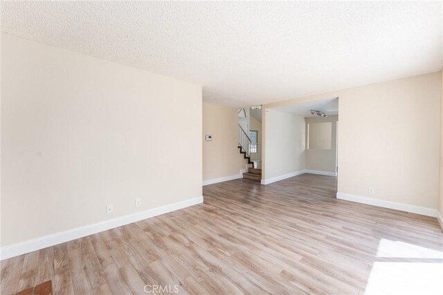 1076 N Ironwood Ave, Rialto, CA 92376 - unfurnished living room featuring baseboards, stairs, a textured ceiling, and light wood finished floors