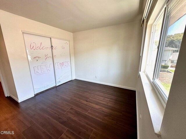 unfurnished bedroom featuring dark wood-style flooring, baseboards, and multiple windows