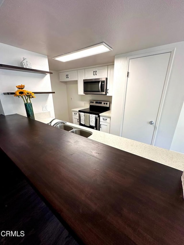 kitchen with a textured ceiling, open shelves, white cabinetry, a sink, and stainless steel appliances