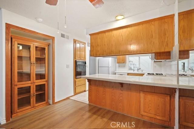 kitchen featuring white appliances, brown cabinetry, a peninsula, visible vents, and light wood finished floors