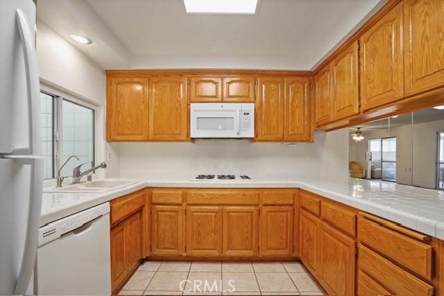 kitchen featuring light countertops, brown cabinets, a sink, and white appliances