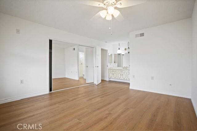 unfurnished bedroom featuring visible vents, baseboards, ensuite bathroom, a ceiling fan, and wood finished floors