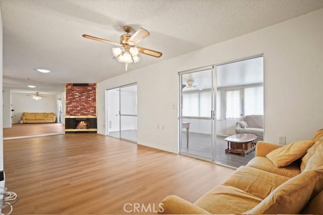 19324 Flowers Ct, Newhall, CA 91321 - living room with a ceiling fan, light wood-type flooring, a fireplace, baseboards, and a textured ceiling