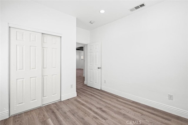 unfurnished bedroom featuring a closet, wood finished floors, baseboards, visible vents, and recessed lighting