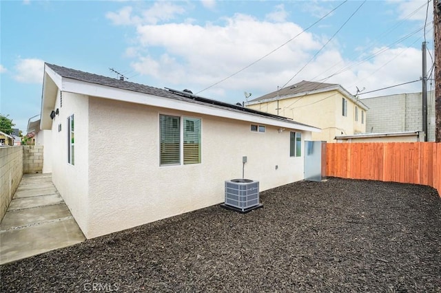 rear view of house featuring stucco siding, central air condition unit, a fenced backyard, and roof mounted solar panels