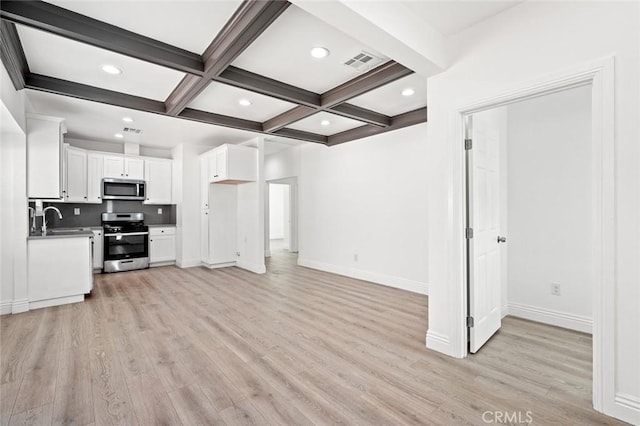 kitchen with light wood finished floors, appliances with stainless steel finishes, visible vents, beamed ceiling, and white cabinets