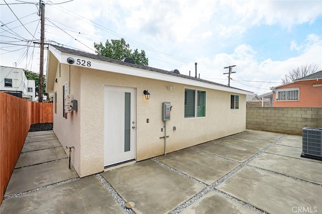 back of property featuring stucco siding, central AC unit, a fenced backyard, and a patio