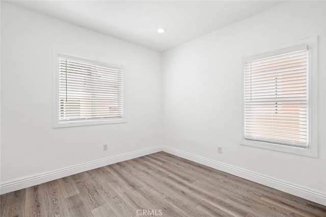 spare room featuring baseboards, wood finished floors, and a healthy amount of sunlight
