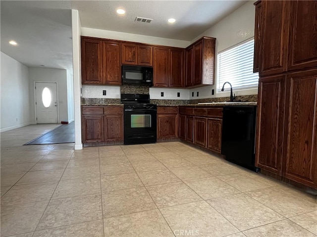kitchen featuring visible vents, black appliances, dark stone countertops, and a sink