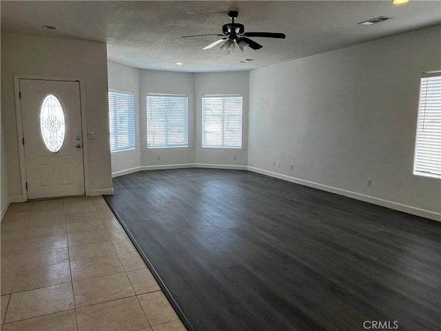 foyer featuring a ceiling fan, a textured ceiling, baseboards, and visible vents