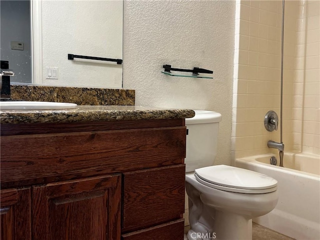 bathroom with bathtub / shower combination, toilet, vanity, and a textured wall