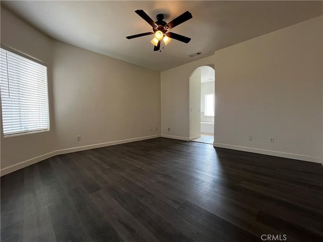 empty room with visible vents, baseboards, a ceiling fan, dark wood finished floors, and arched walkways