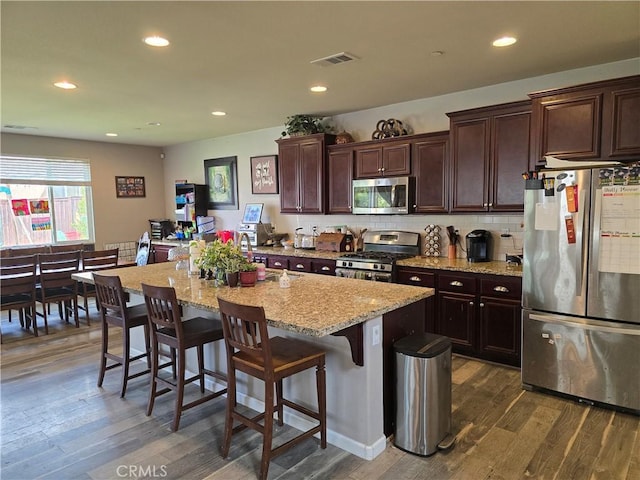 30130 Pine Needle Rd, Menifee, CA 92585 - kitchen featuring appliances with stainless steel finishes, dark wood-style floors, an island with sink, a kitchen breakfast bar, and dark brown cabinets