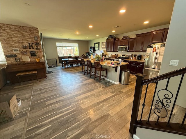30130 Pine Needle Rd, Menifee, CA 92585 - kitchen with appliances with stainless steel finishes, dark brown cabinets, wood finished floors, a breakfast bar, and a center island with sink