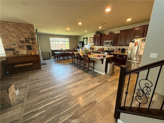 30130 Pine Needle Rd, Menifee, CA 92585 - kitchen featuring appliances with stainless steel finishes, dark brown cabinetry, wood finished floors, a kitchen bar, and an island with sink