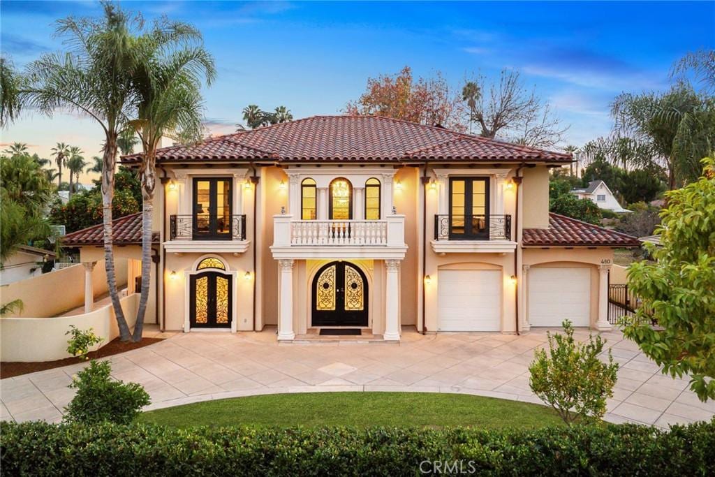 mediterranean / spanish house with a tiled roof, french doors, fence, and a balcony
