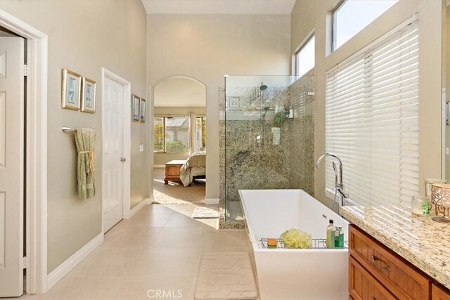 full bathroom with a stall shower, a freestanding tub, baseboards, a high ceiling, and vanity